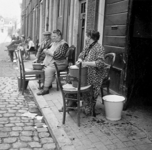 876864 Gezicht in de Koningstraat in Wijk C te Utrecht, waar twee vrouwen aardappelen aan het schillen zijn voor hun ...